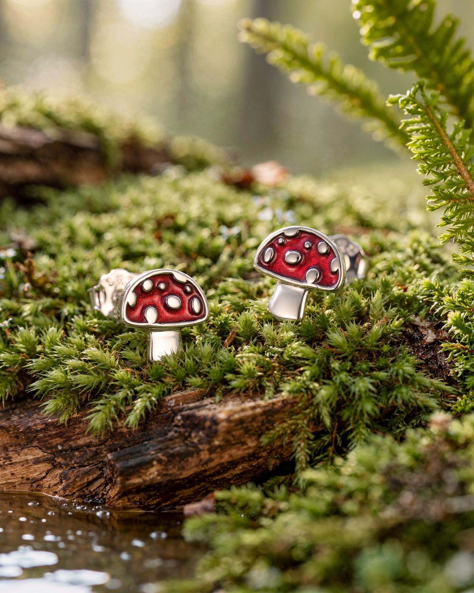 Sterling silver red enamel mushroom stud earrings displayed on moss in a woodland scene