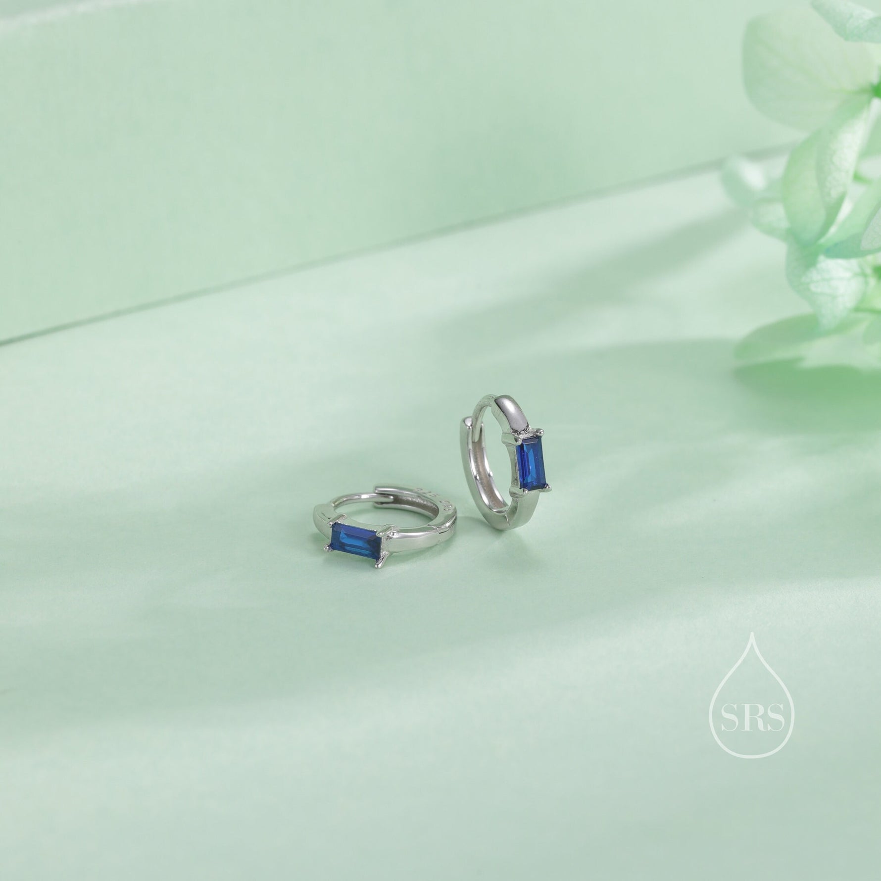 May include: A pair of silver hoop earrings with a small blue rectangular gemstone on each hoop.
