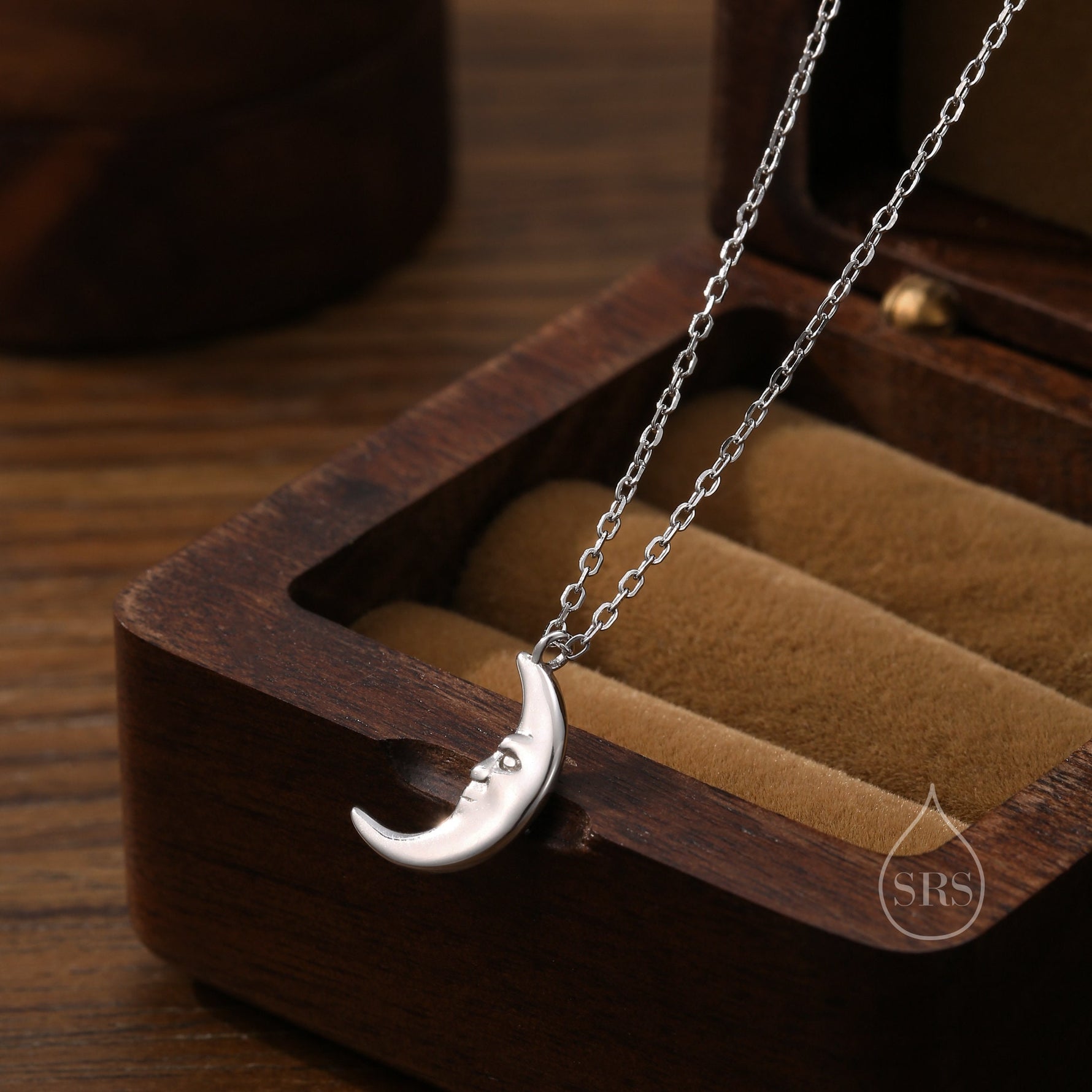 May include: A silver crescent moon necklace with a detailed face on the moon pendant. The necklace is displayed in a wooden box.