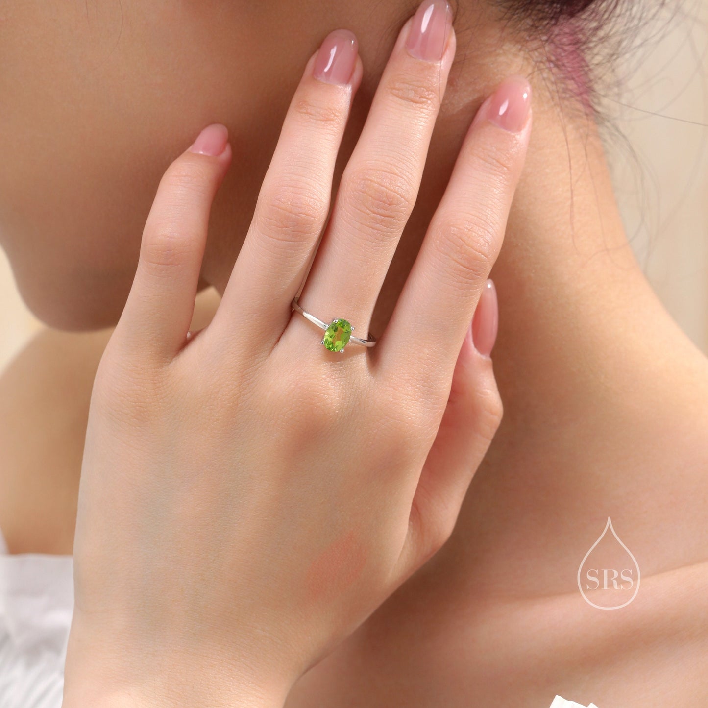 May include: A silver ring featuring a green oval gemstone. The ring is worn on a person's finger.