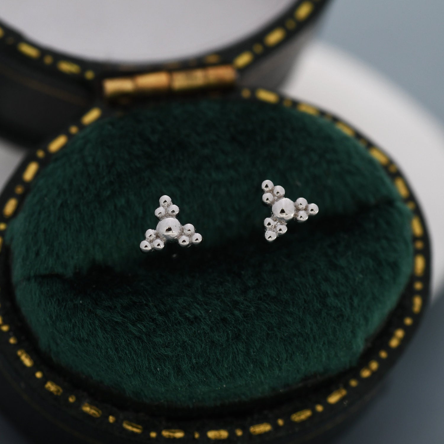 May include: A pair of silver triangle stud earrings with a textured surface. The earrings are displayed in a green velvet jewellery box.
