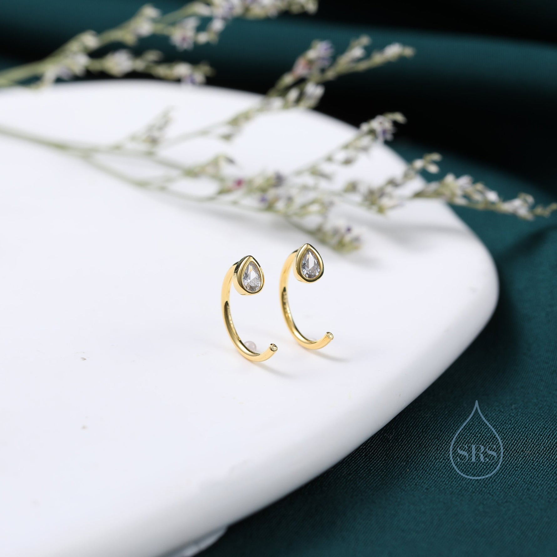 May include: A pair of gold hoop earrings with a teardrop-shaped clear crystal in the centre of each hoop.