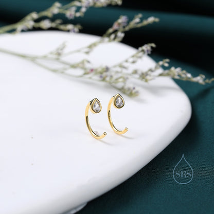 May include: A pair of gold hoop earrings with a teardrop-shaped clear crystal in the centre of each hoop.