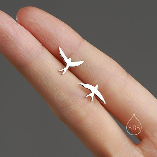May include: A pair of silver earrings featuring a minimalist design of two small birds in flight.