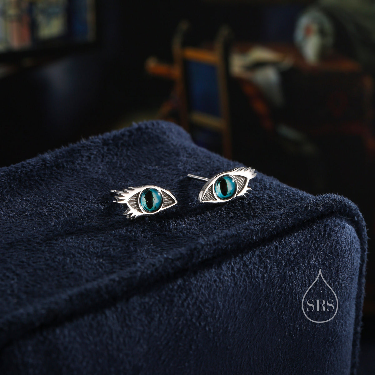 May include: A pair of silver earrings featuring a detailed eye design. The eyes are blue with a silver iris and pupil.
