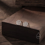 May include: A pair of silver stud earrings featuring a pentagram design. The earrings are displayed on a wooden surface.