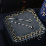 May include: A pair of silver chain earrings with black gemstone accents. The earrings are displayed in a blue velvet box with gold trim.