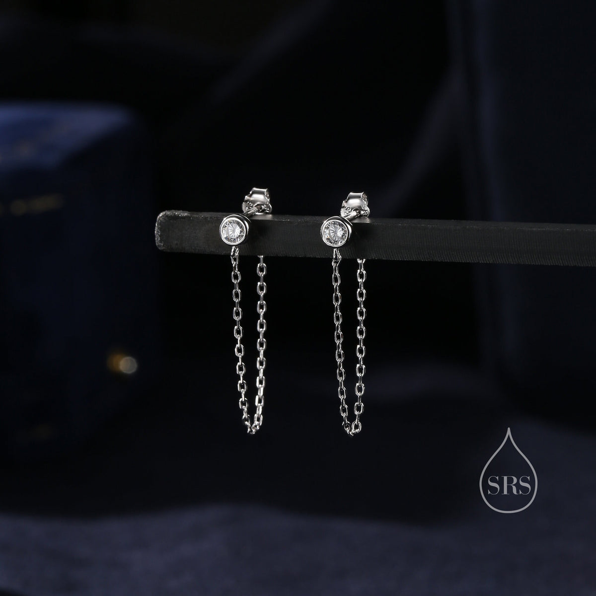 May include: A pair of silver earrings with a small clear stone and a dangling chain.