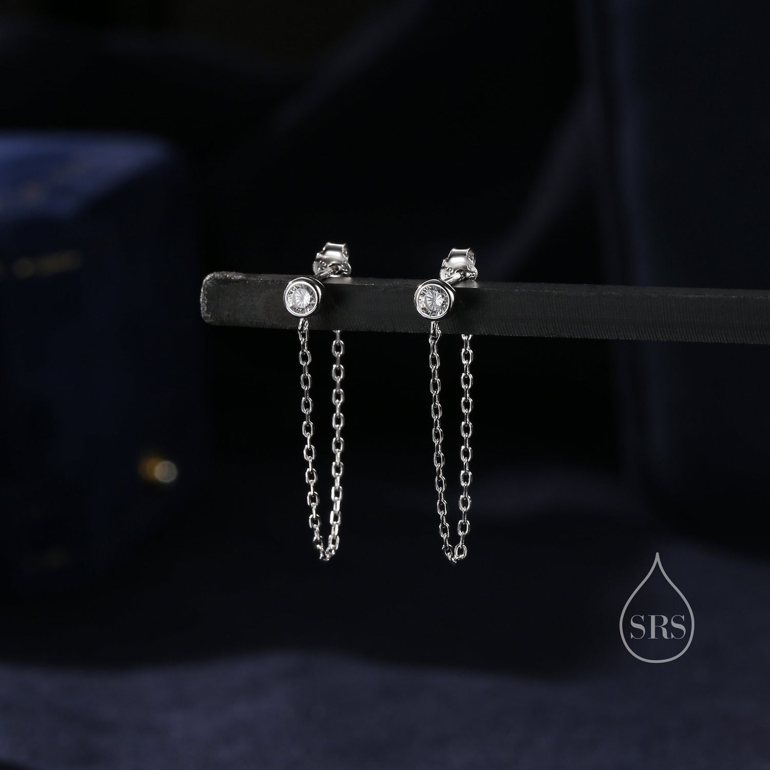 May include: A pair of silver earrings with a small clear stone and a dangling chain.