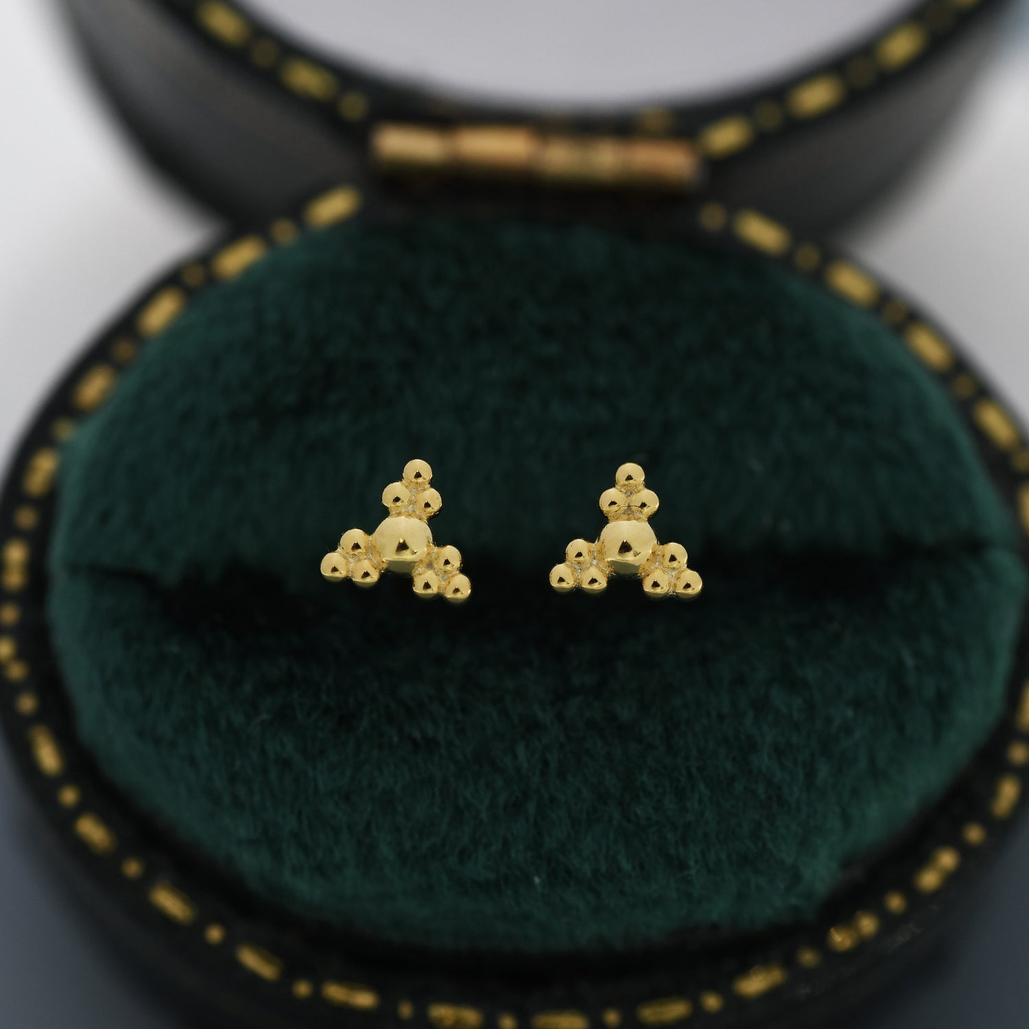 May include: A pair of gold triangle stud earrings with a textured surface. Each triangle is made up of small, round beads.