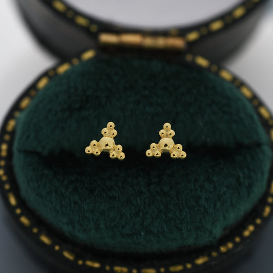 May include: A pair of gold triangle stud earrings with a textured surface. Each triangle is made up of small, round beads.