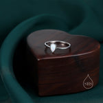 May include: A silver ring featuring a teardrop-shaped white opal gemstone. The ring is presented in a heart-shaped wooden box.