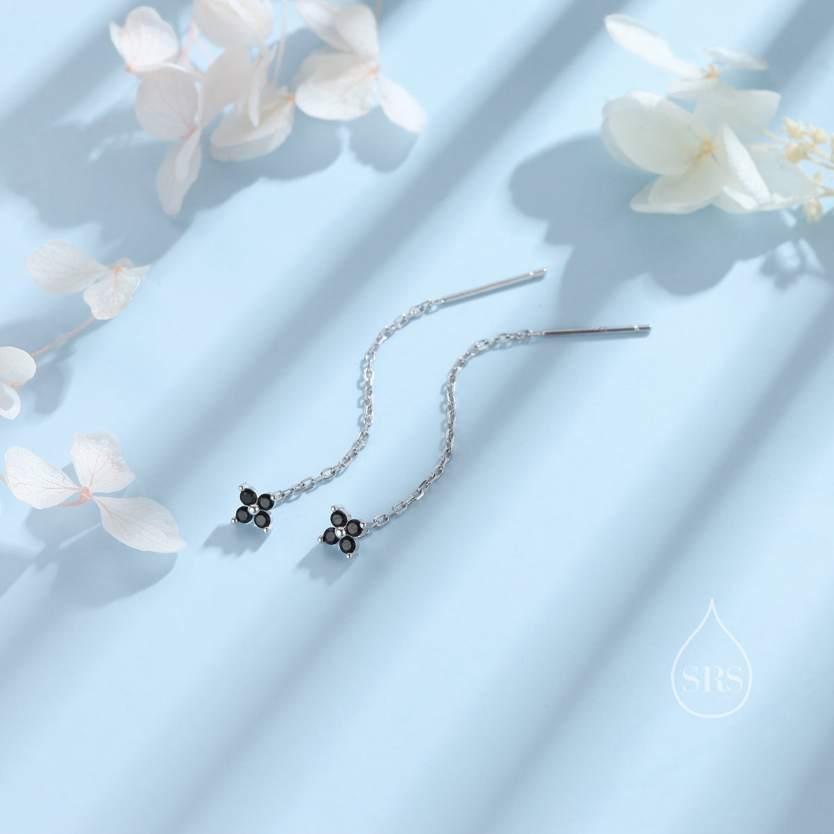 May include: A pair of silver dangle earrings with a small black flower charm at the end of each chain.