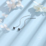 May include: A pair of silver dangle earrings with a small black flower charm at the end of each chain.