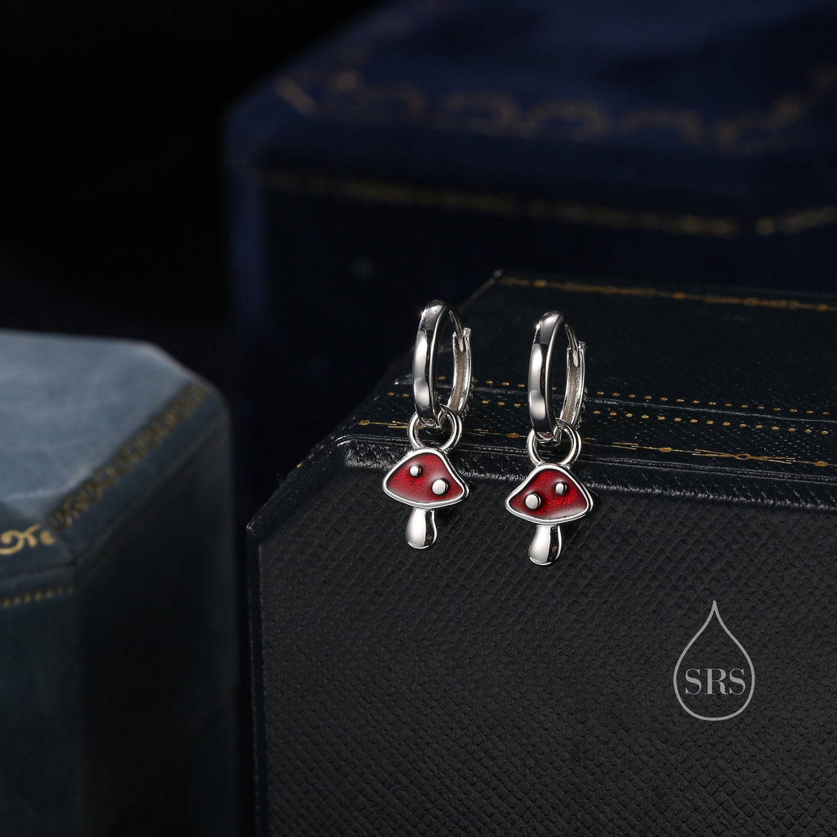 May include: A pair of silver hoop earrings with red mushroom charms. The mushrooms have white stems and white dots on the red caps.