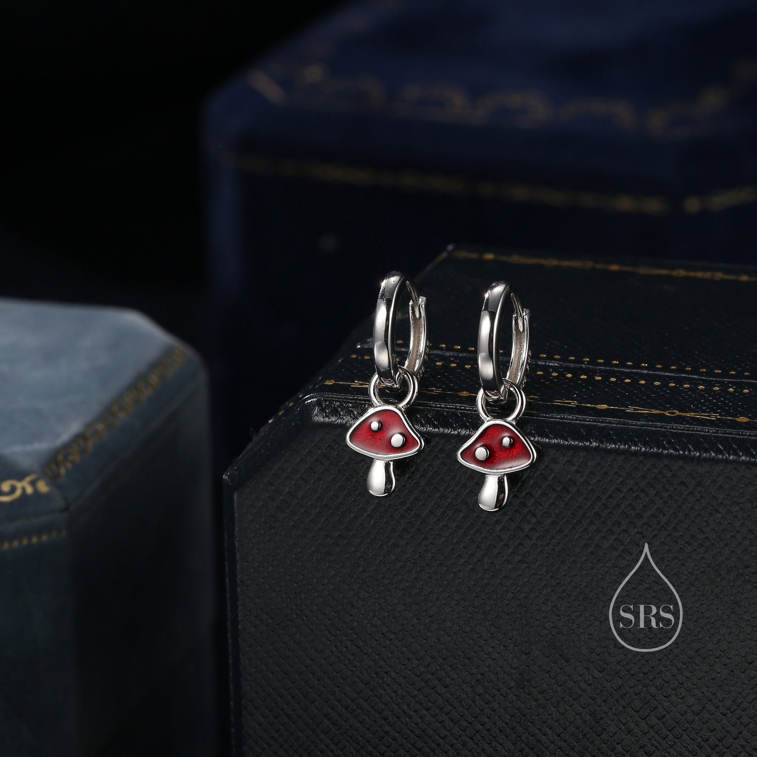 May include: A pair of silver hoop earrings with red mushroom charms. The mushrooms have white stems and white dots on the red caps.