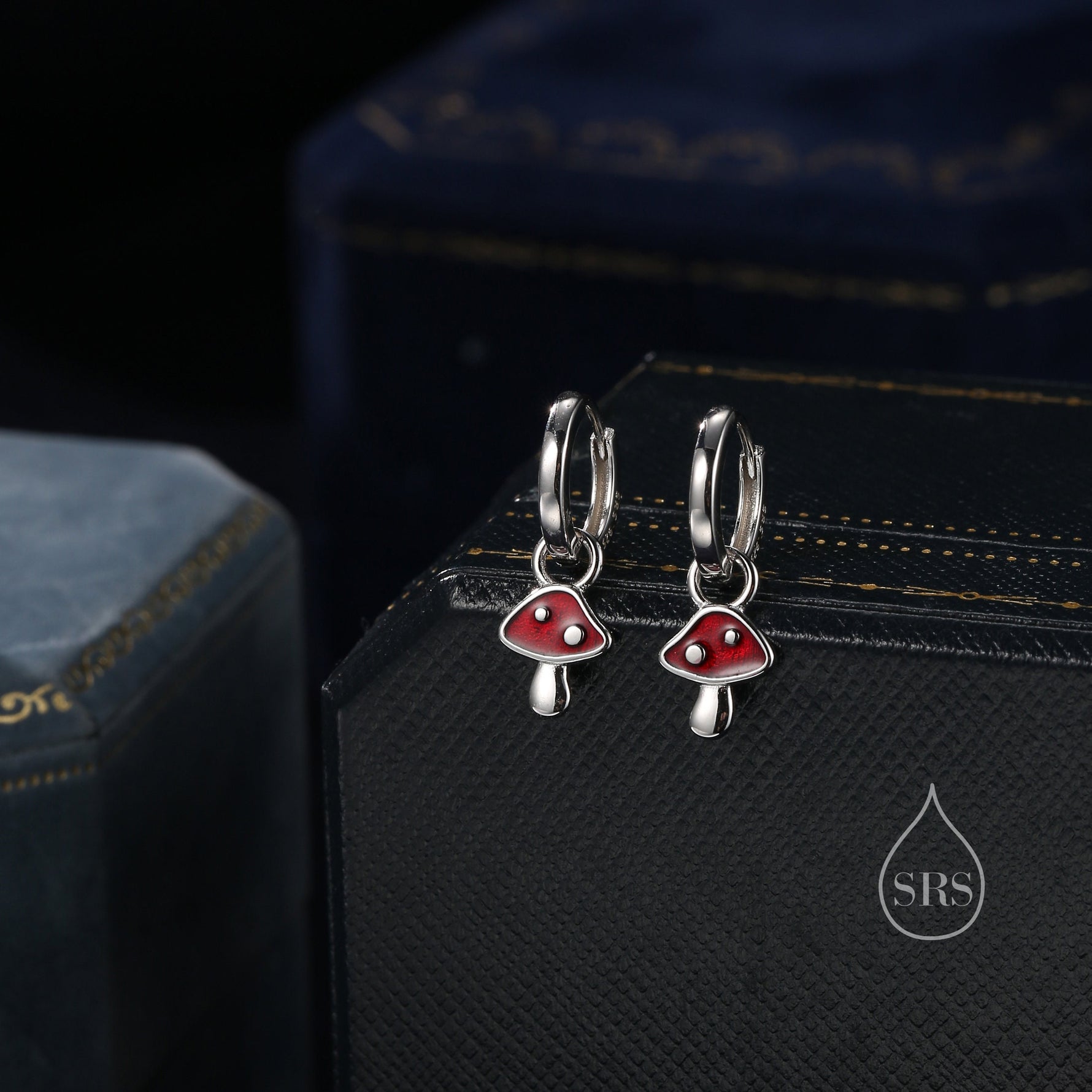 May include: A pair of silver hoop earrings with red mushroom charms. The mushrooms have white stems and white dots on the red caps.