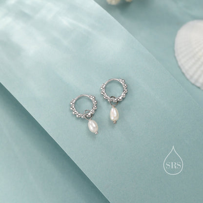 May include: A pair of silver hoop earrings with a small pearl dangling from each hoop. The earrings are on a light blue background.