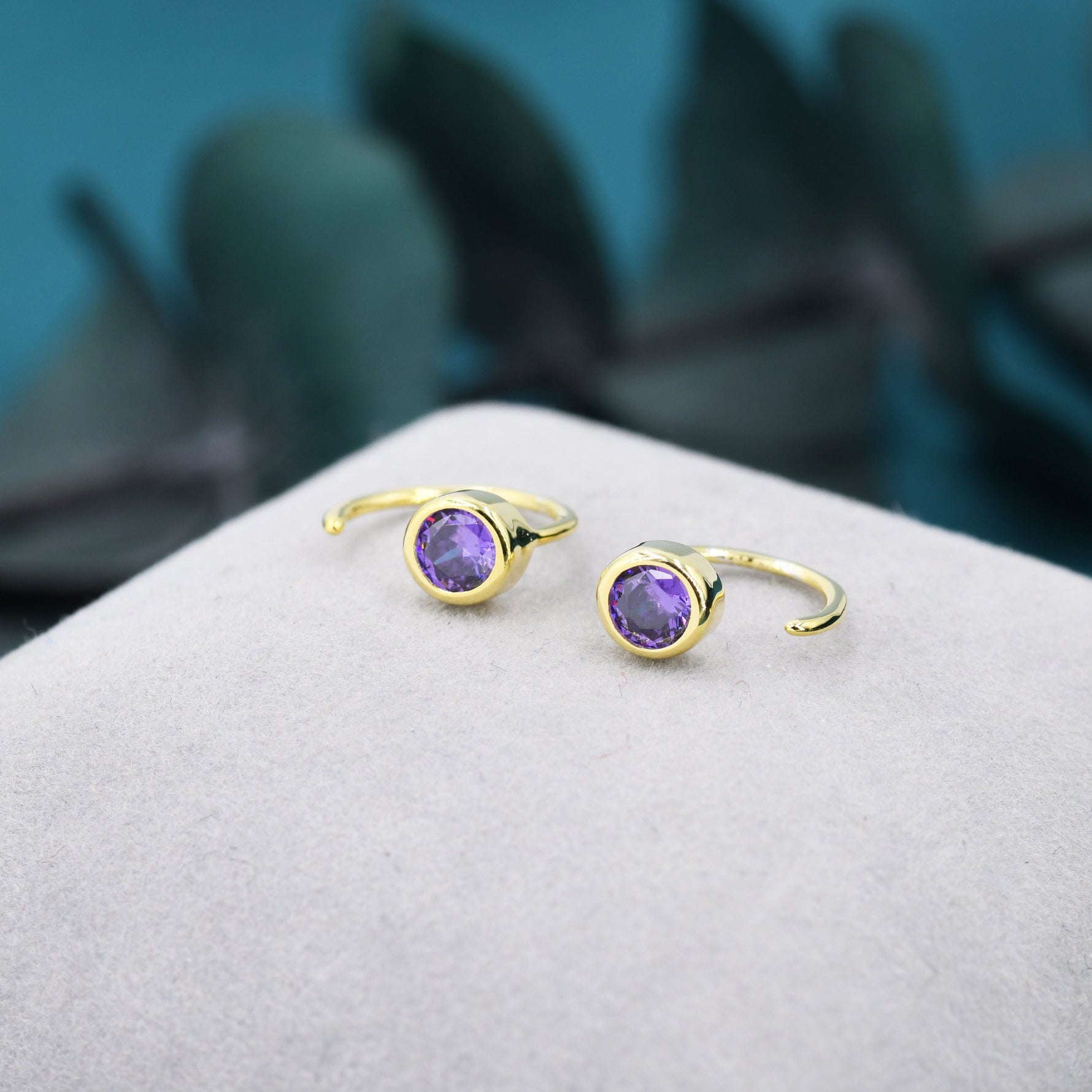May include: A pair of gold hoop earrings with a purple gemstone in the centre of each hoop.