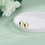 May include: A pair of gold hoop earrings with black rectangular stones. The earrings are on a white surface.