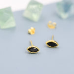 May include: A pair of gold earrings with black oval-shaped stones. The earrings are on a light blue surface.