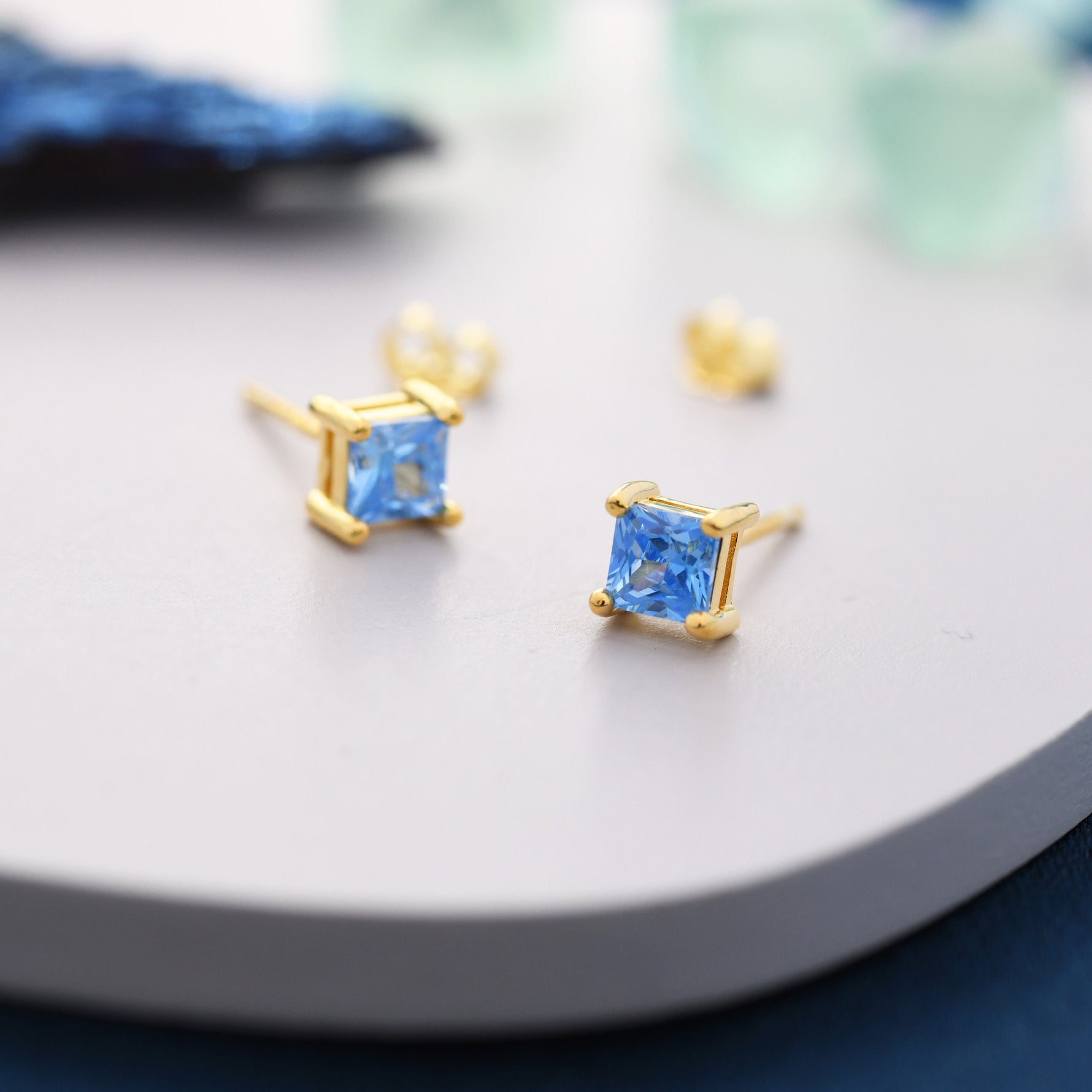 May include: A pair of gold square stud earrings with light blue square-shaped gemstones.
