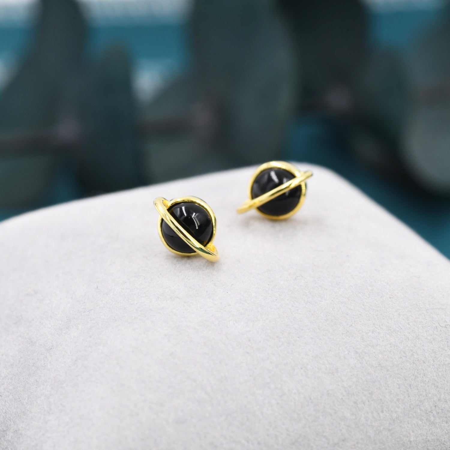 May include: A pair of gold-toned earrings with black round stones set in a ring design. The earrings are on a white surface.