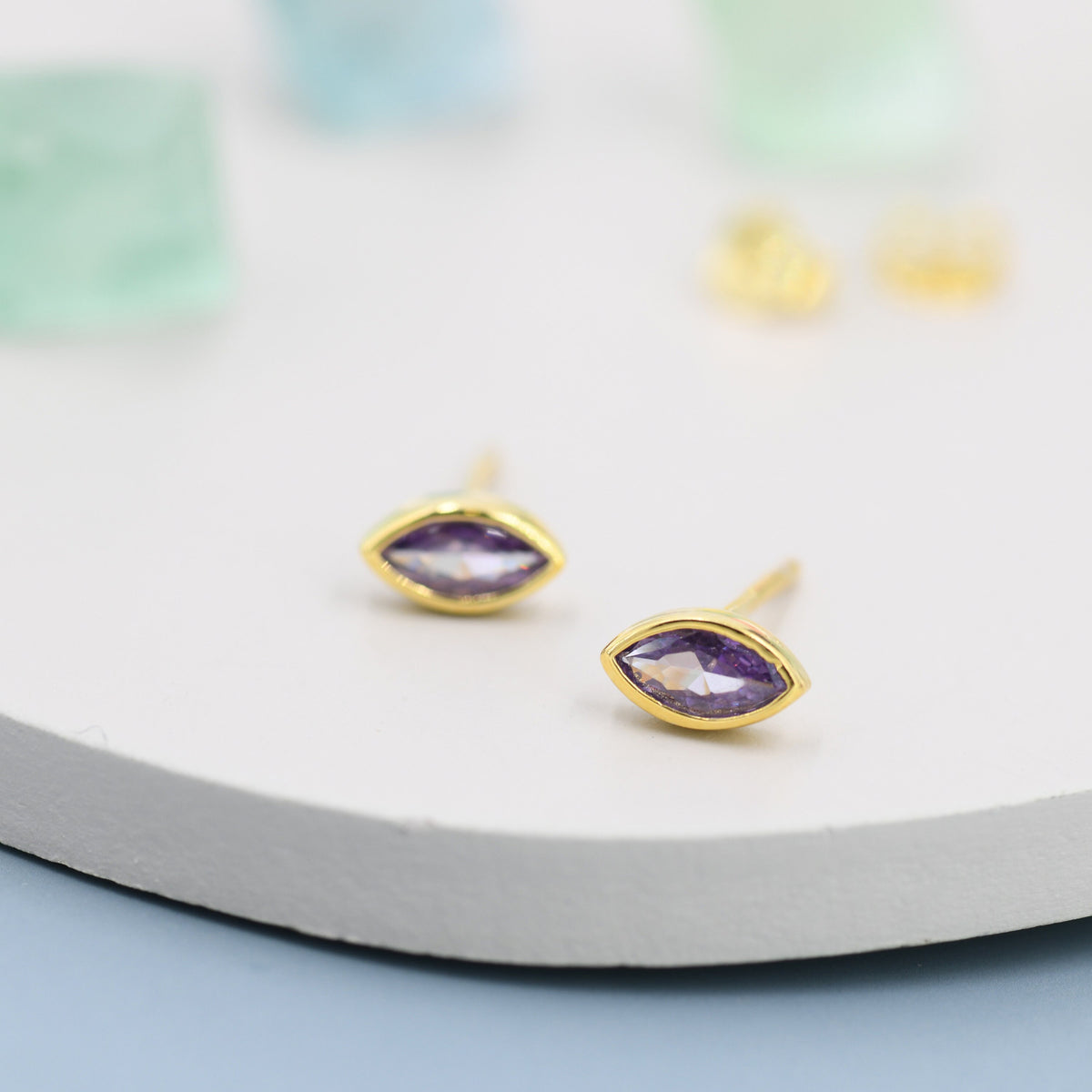 May include: A pair of gold earrings with purple marquise-shaped gemstones.