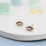 May include: A pair of gold earrings with purple marquise-shaped gemstones.