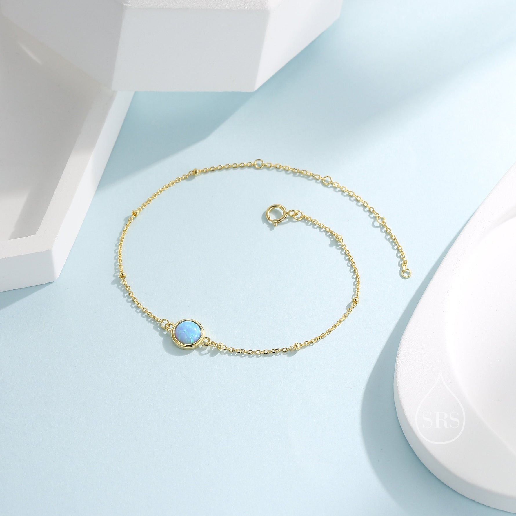 May include: A delicate gold chain bracelet featuring a round opal gemstone pendant. The bracelet has a fine chain with small beads and a lobster clasp.
