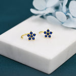 May include: A pair of gold flower-shaped earrings with blue gemstones. The earrings are on a white surface.