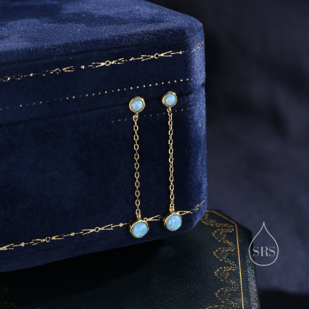May include: A pair of delicate gold earrings with a small blue opal stone dangling from each chain.