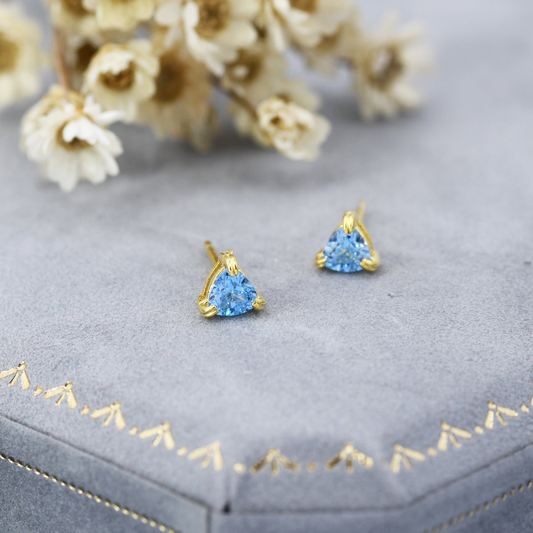 May include: A pair of gold stud earrings with a triangular blue gemstone in the centre of each earring.