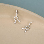 May include: A pair of silver-toned stud earrings shaped like a chemical molecular structure. Each earring features a central hexagonal ring connected to a short chain of three circular nodes, creating a distinct scientific representation in polished metal.